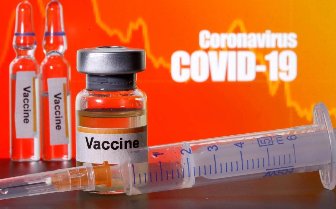 Small bottles labeled with Vaccine stickers stand near a medical syringe in front of displayed Coronavirus COVID 19 words in this illustration